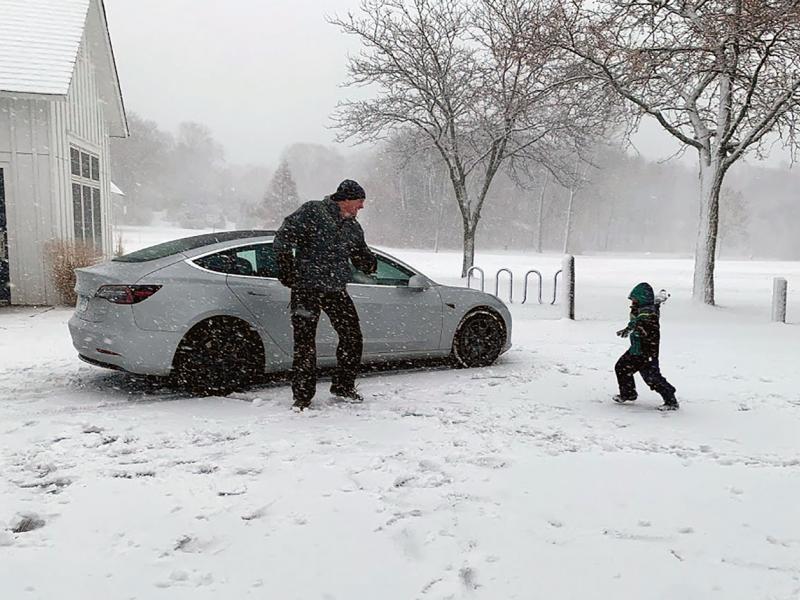 Dad and kid play in snow near parked car