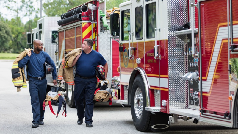 Two male firefighters walking next to fire truck
