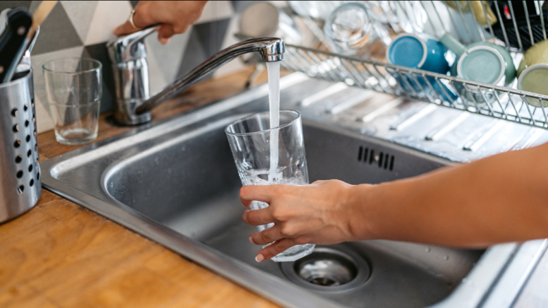 a hand filling a water glass at a kitchen sink