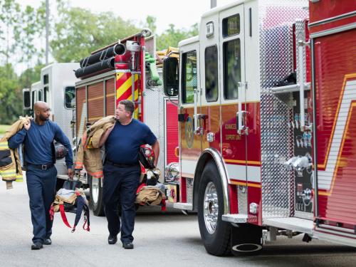 Two male firefighters walking next to fire truck