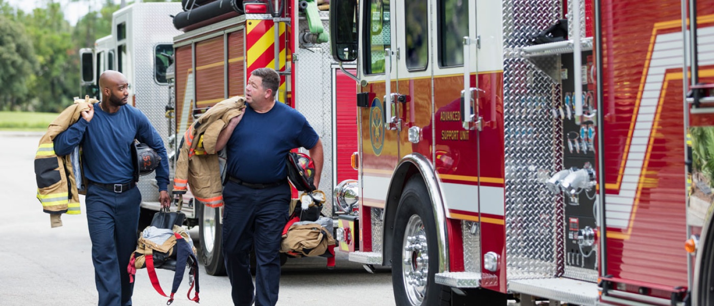 Two male firefighters walking next to fire truck