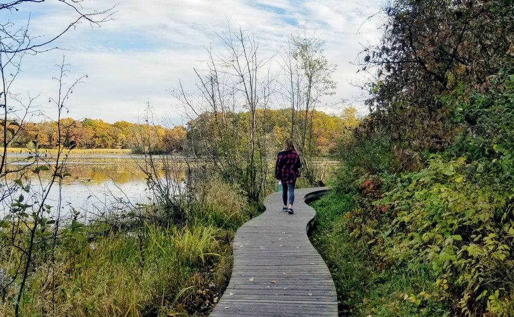 woman walks along boardwalk next to lake