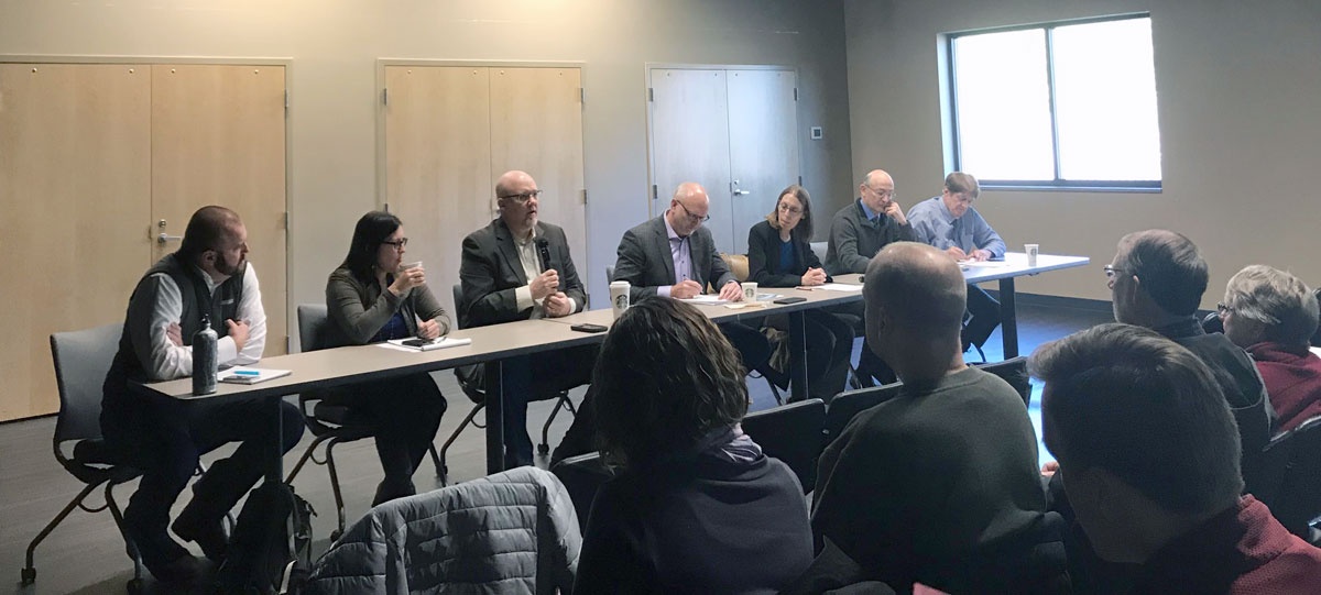 Seven people sit at panel table in front of audience