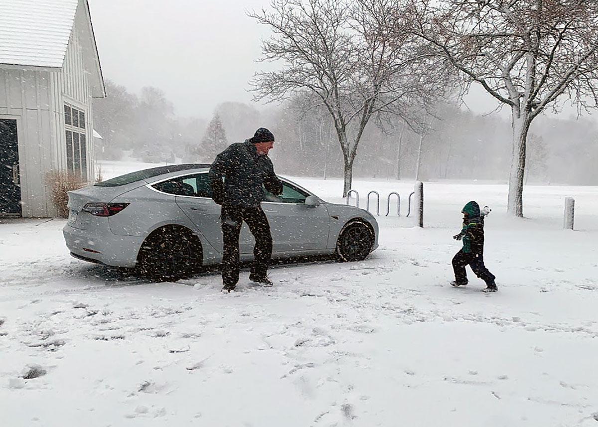 Dad and kid play in snow near parked car