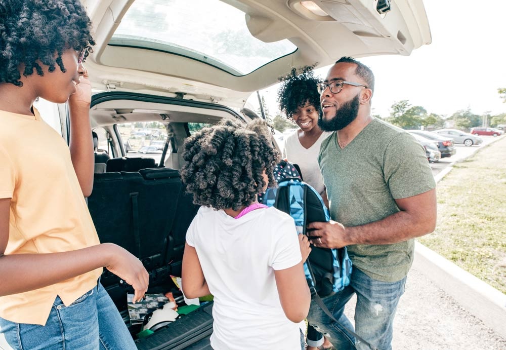 family puts backpacks into trunk of car