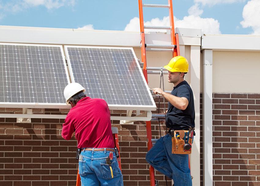 Two workers on ladders install solar panels on building