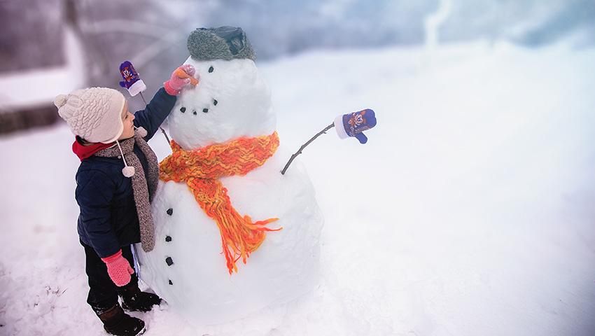 Kid places carrot nose on snowman