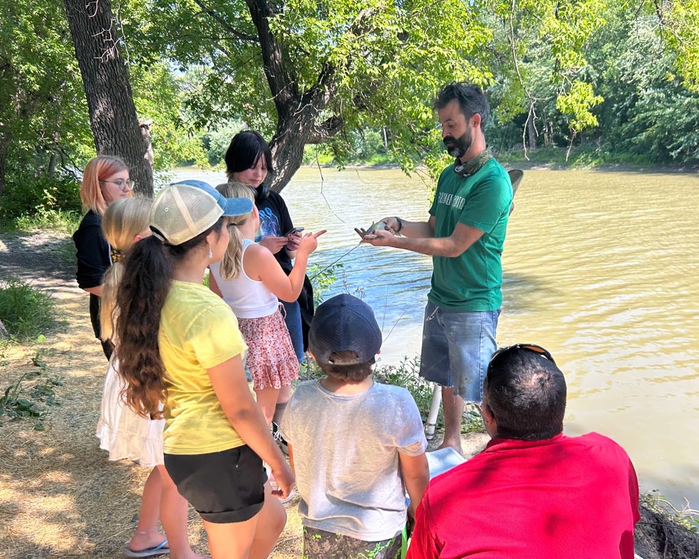 Adult teaches group of kids how to fish