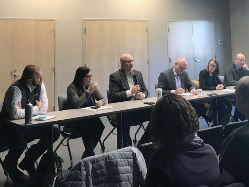 Seven people sit at panel table in front of audience