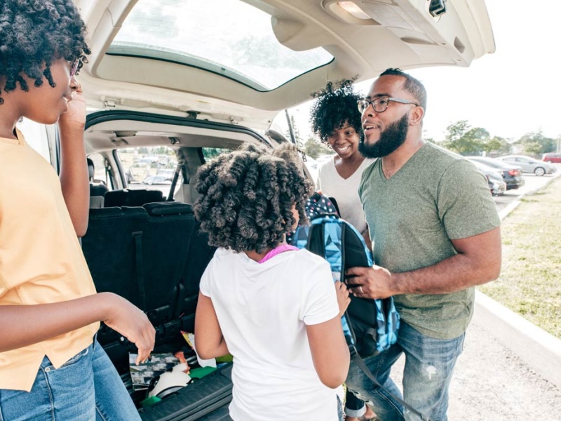 family puts backpacks into trunk of car