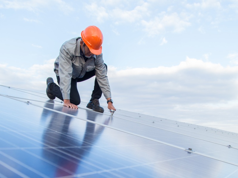 Worker in hard hat works on solar panel