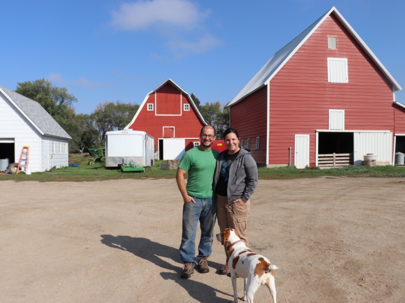 Farmer couple with their dog on by their barn