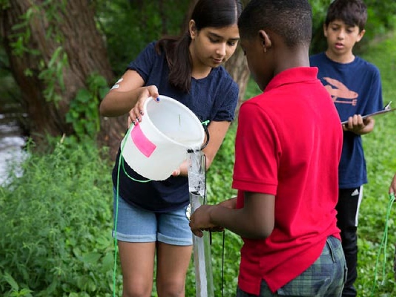 Kids pour water from a bucket into a container